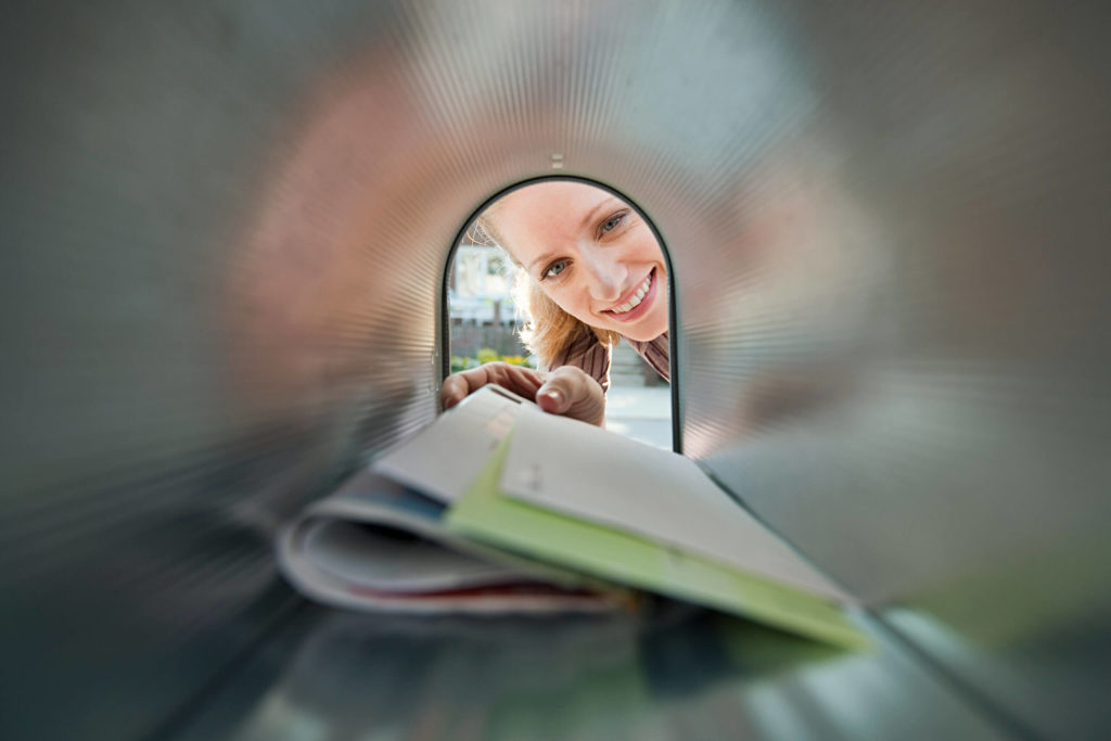 Direct mail marketing remains an effective print advertising tool, and it has seen a resurgence as a result of the COVID-19 pandemic. This is an artistic image of a woman pulling mail out of a mailbox.
